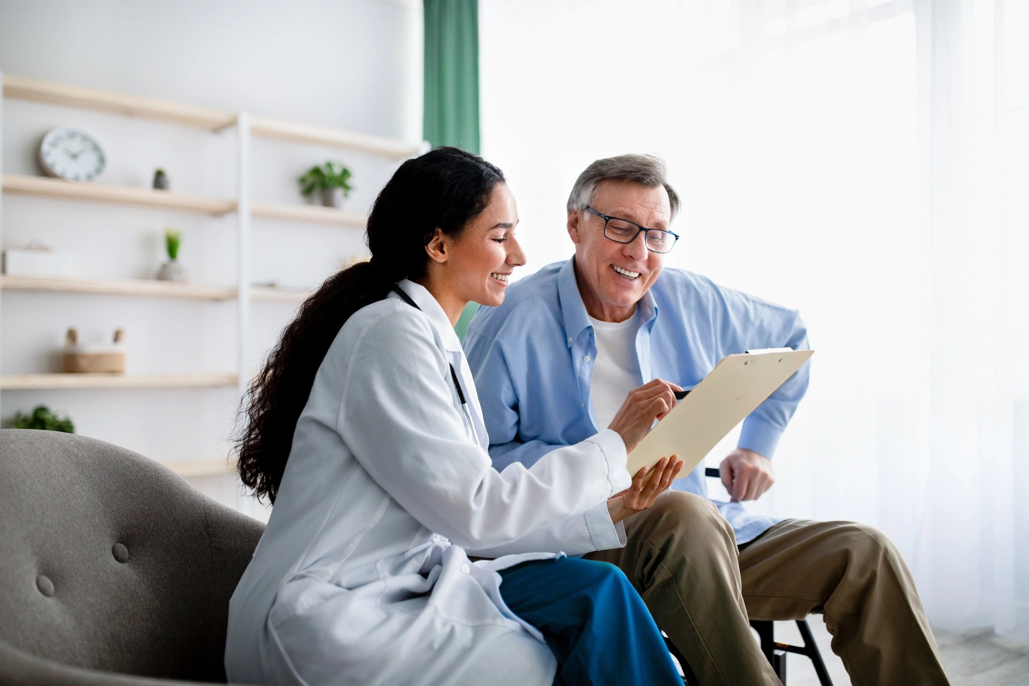 A doctor smiling and discussing a clipboard with an elderly man.