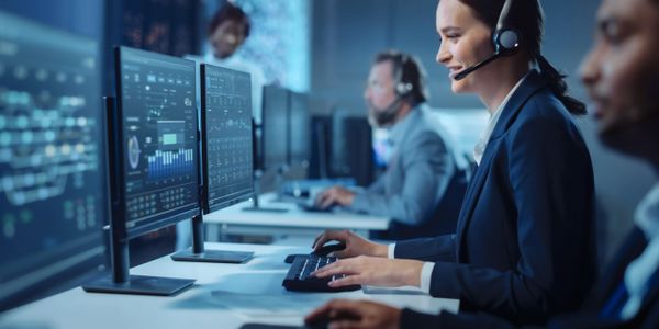 Call center employees working with headsets and multiple monitors.