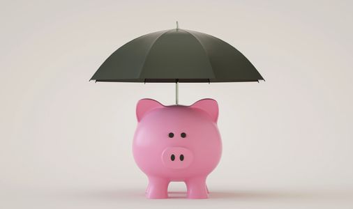 Pink piggy bank protected by a green umbrella on a plain background.