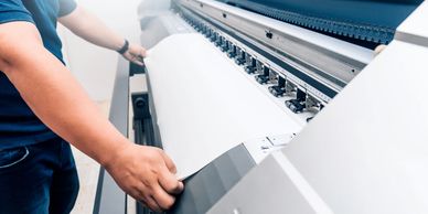 Person feeding large sheet into an industrial printer.