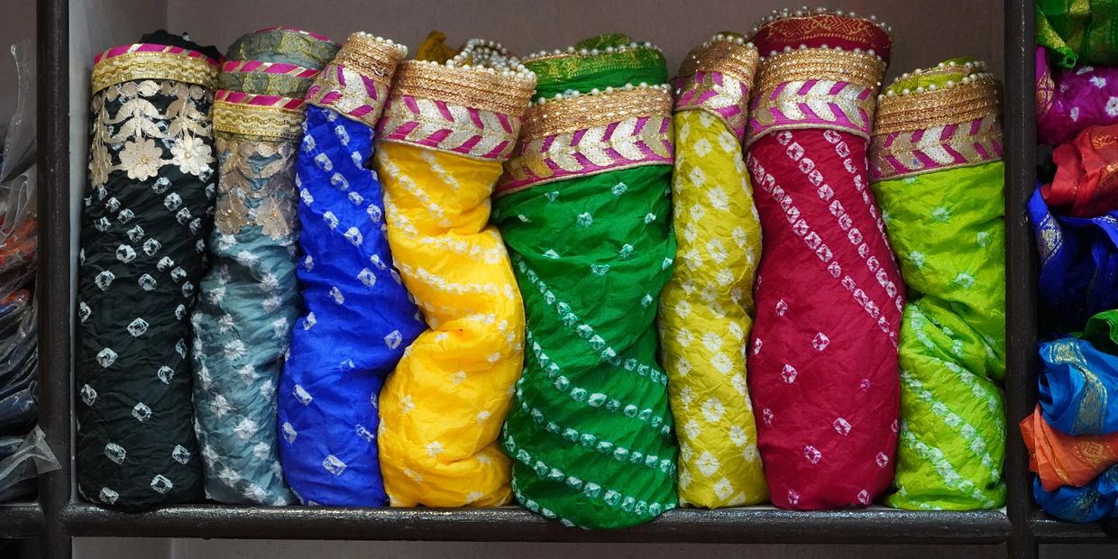 Colorful folded fabrics with intricate patterns neatly arranged on a shelf.