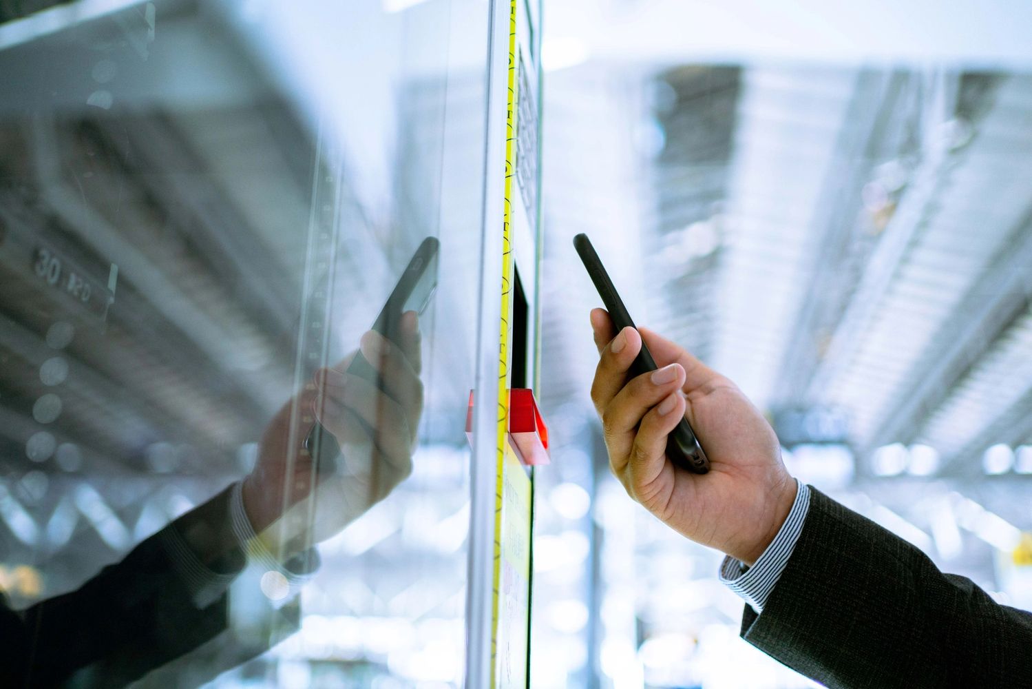 A person in a suit using a smartphone near a reflective board in a modern building.