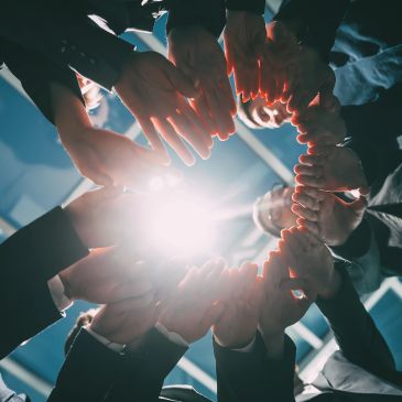 People forming a circle with their hands around a bright light.