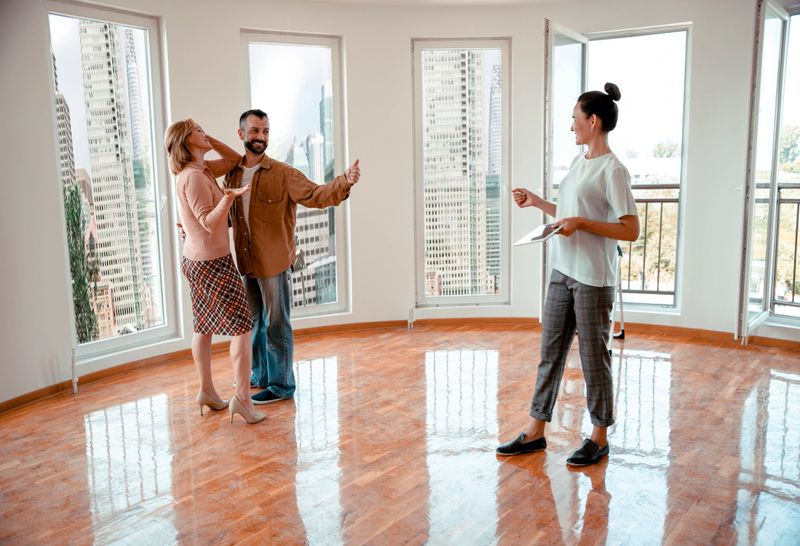 Happy adult couple with estate agent in new home living room. Husband and wife Viewing apartment for their property investment