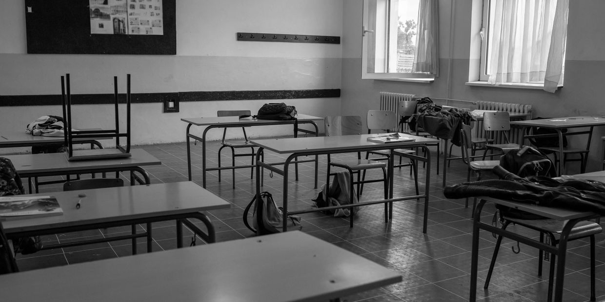Empty classroom with scattered backpacks and jackets on desks and chairs.