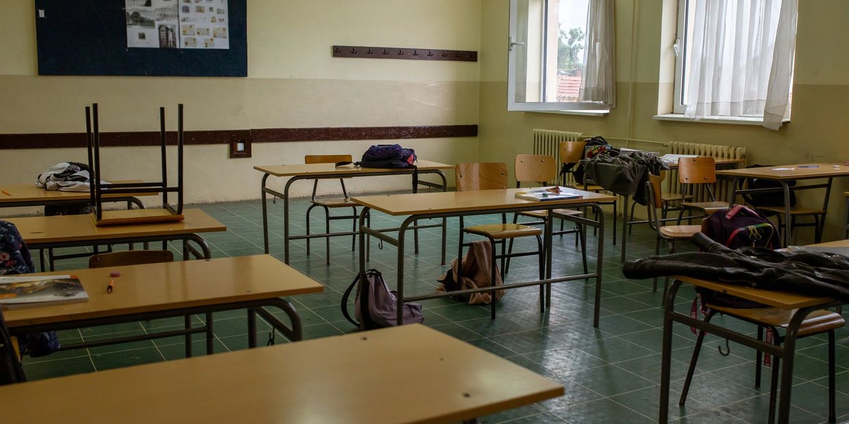 Empty classroom with scattered backpacks and jackets on desks and chairs.