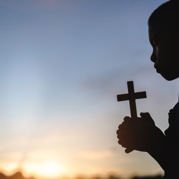 Silhouette of a person holding a cross at sunset.