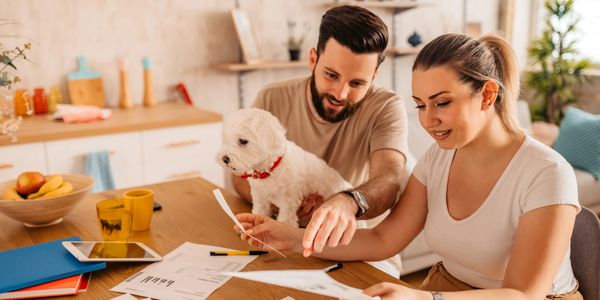 Couple with a dog reviewing documents at a wooden table in a cozy kitchen.