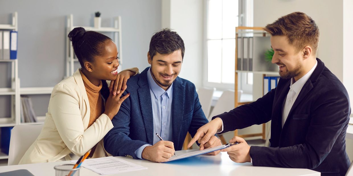 A couple signing documents with a smiling professional.