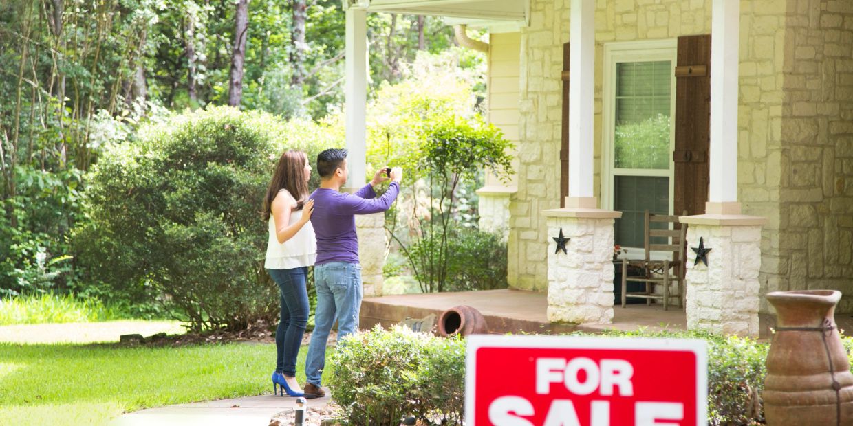 Couple examining a house for sale in a lush neighborhood.