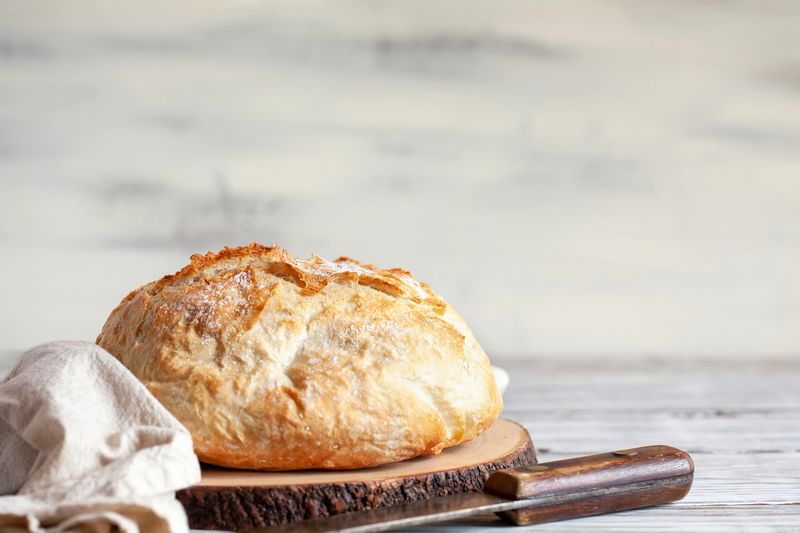 Fresh homemade artisan bread on a cutting board with tea towel and knife.