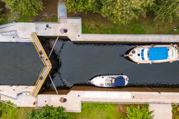 Aerial view of boats passing through a canal lock with concrete walls and green surroundings.