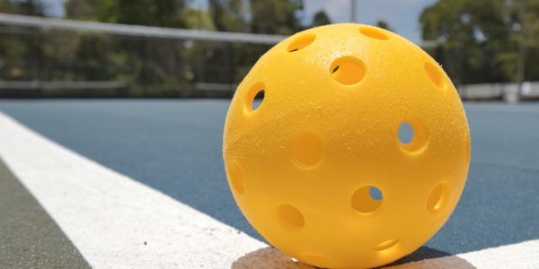 Outdoor pickleball game setup with yellow balls and blue court.

