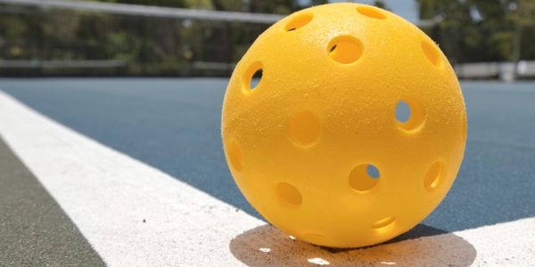 Outdoor pickleball game setup with yellow balls and blue court.

