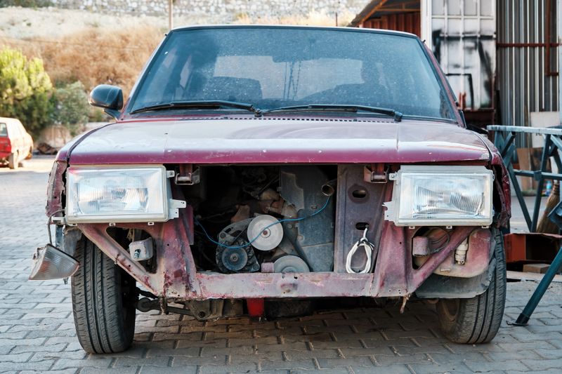Front view of an old abandoned car with missing parts at the junkyard.