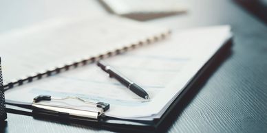 Close-up of paperwork on a clipboard with a pen on a dark wooden desk.