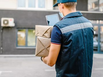 Delivery worker holding packages and checking a tablet outdoors.