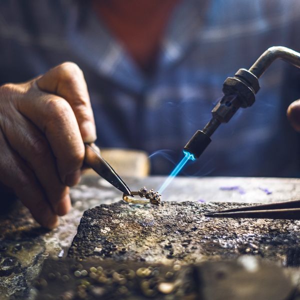 A jeweler soldering a ring using a blue flame torch.