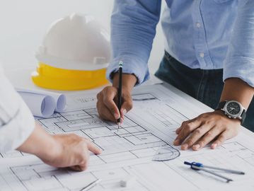 Architects reviewing and marking building blueprints on a desk with construction helmets nearby.