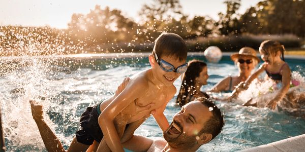 A joyful family plays and splashes in a sunlit swimming pool.