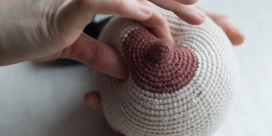 Hand touching a crocheted breast model.