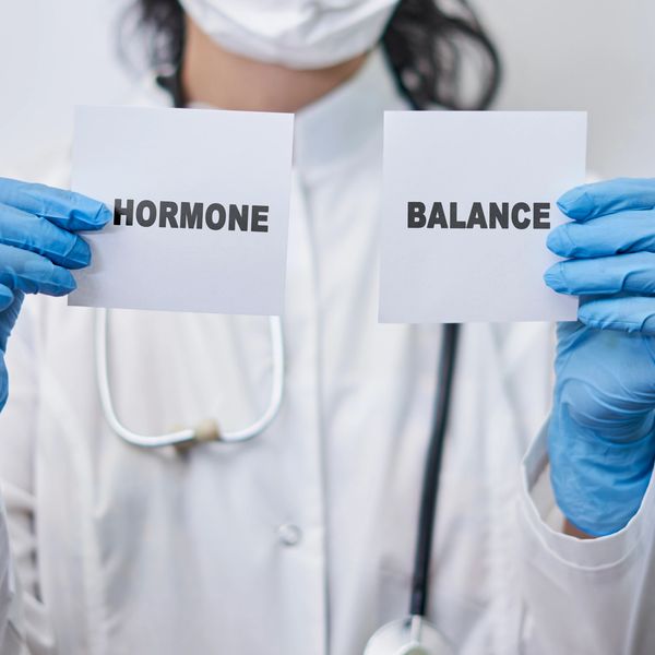 Medical professional holding cards reading 'HORMONE' and 'BALANCE'.