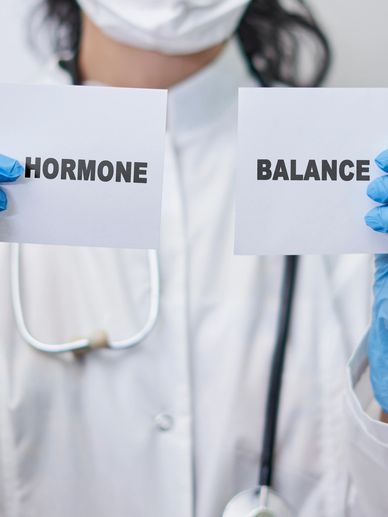 Medical professional holding cards reading 'HORMONE' and 'BALANCE'.