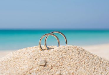 Two silver wedding rings standing in the sand near the sea.