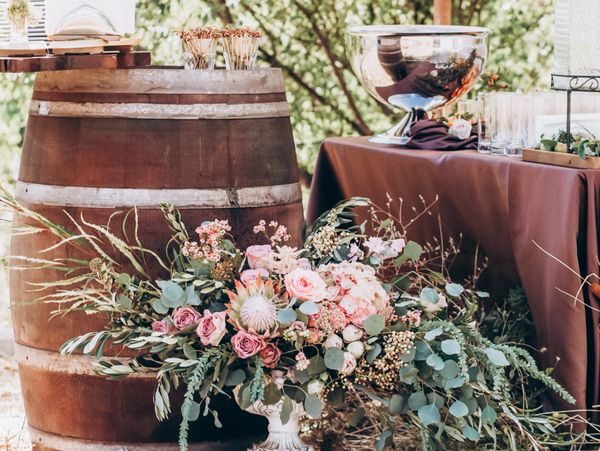 Rustic wedding decor with flowers, a barrel, and a table setting outdoors.