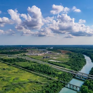 Aerial view of a river, green fields, and highways under a blue sky with clouds.