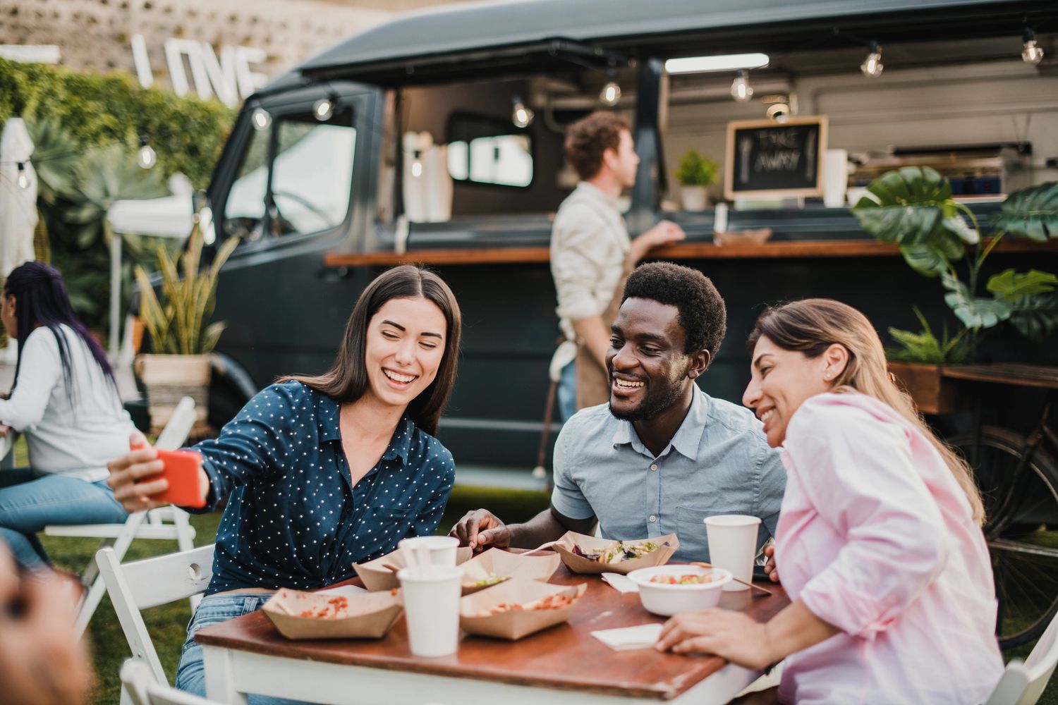 Three friends smiling and taking a selfie at an outdoor food truck event.