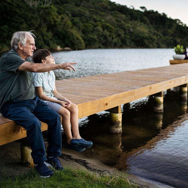 An elderly man and a child sitting on a wooden dock by the water.