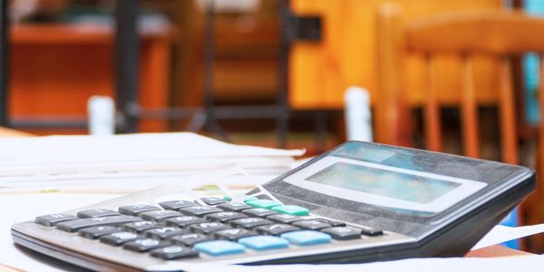 Calculator on a desk with papers and a wooden chair in the background.