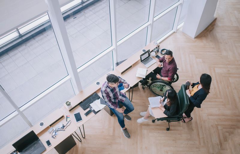 directly above Indian male in wheelchair leading coworker group discussion in creative office