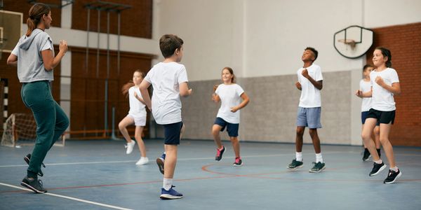 Children exercising in a gym under instructor supervision.