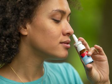Woman using a nasal spray outdoors.