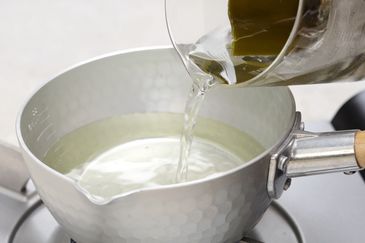 Water is being poured into a hammered metal pot on a stove.