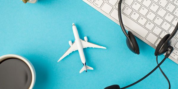 Workspace with airplane model, headset, keyboard, coffee, and plant on blue background.