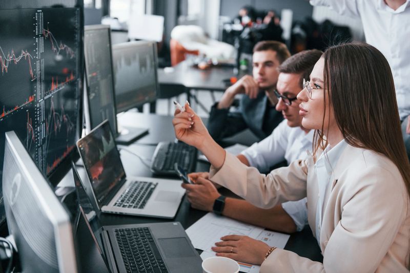 Analysing information. Team of stockbrokers works in modern office with many display screens.