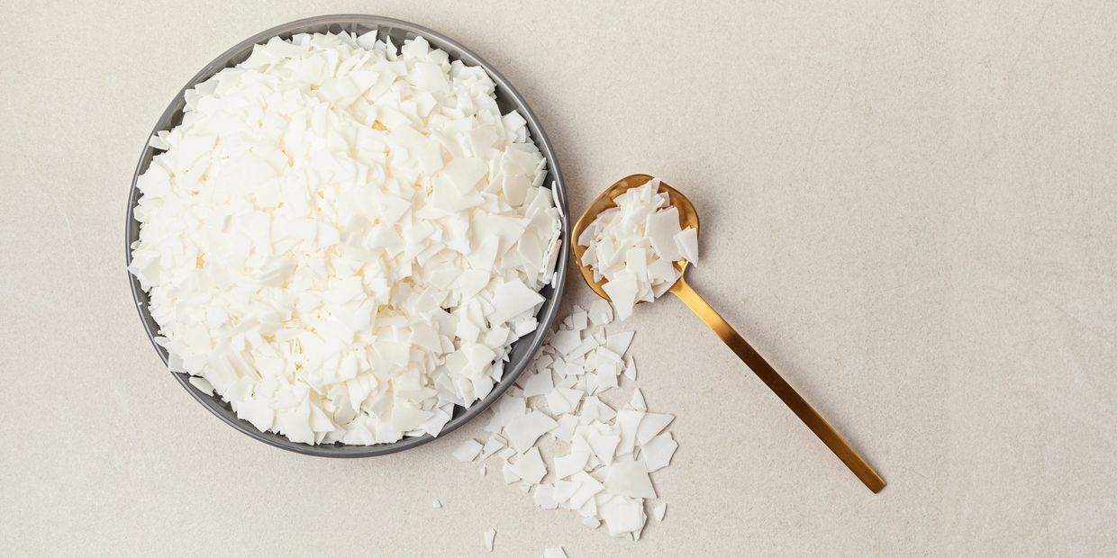 White wax flakes in a bowl and on a golden spoon on a beige surface.