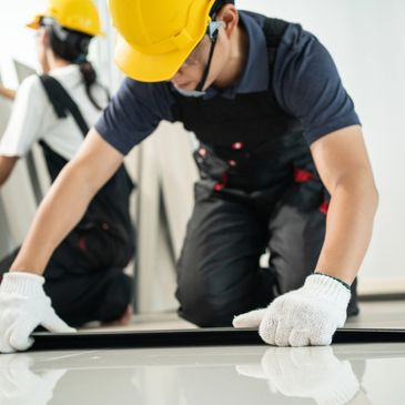 Workers in safety gear installing flooring panels indoors.
