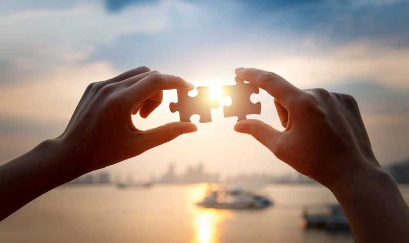 Human hands put two jigsaw puzzle pieces together.