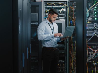 Tech professional working on laptop in server room.