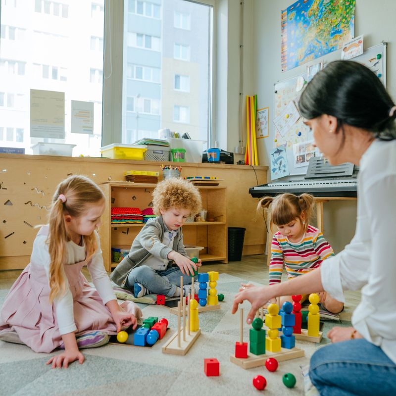 Preschool students sorting wooden geometric toy balls and cubes sittings on the floor. Learning toys in kindergarten or daycare centre. Education concept. Selective focus.