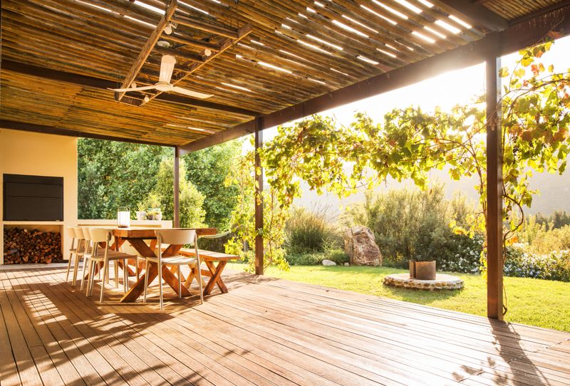 Patio table and chairs sitting next to a barbecue outside on a rustic wooden balcony on a sunny afternoon