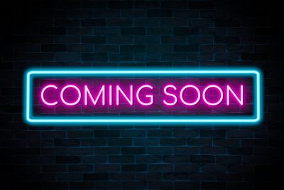 Neon sign reading 'COMING SOON' against a dark brick wall.
