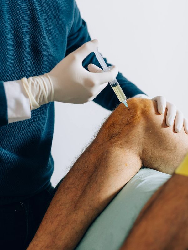 Medical professional injecting a patient's knee with a syringe.
