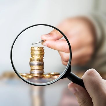 Magnifying glass focusing on stacked coins with a hand adding a coin.