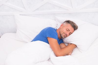 Man sleeping in bed peacefully with white sheets and pillows after using medical marijuana for a sleep aid