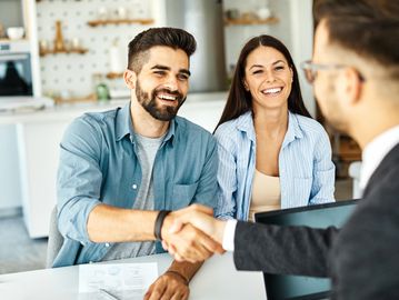 A happy couple shaking hands with a professional in a modern office.